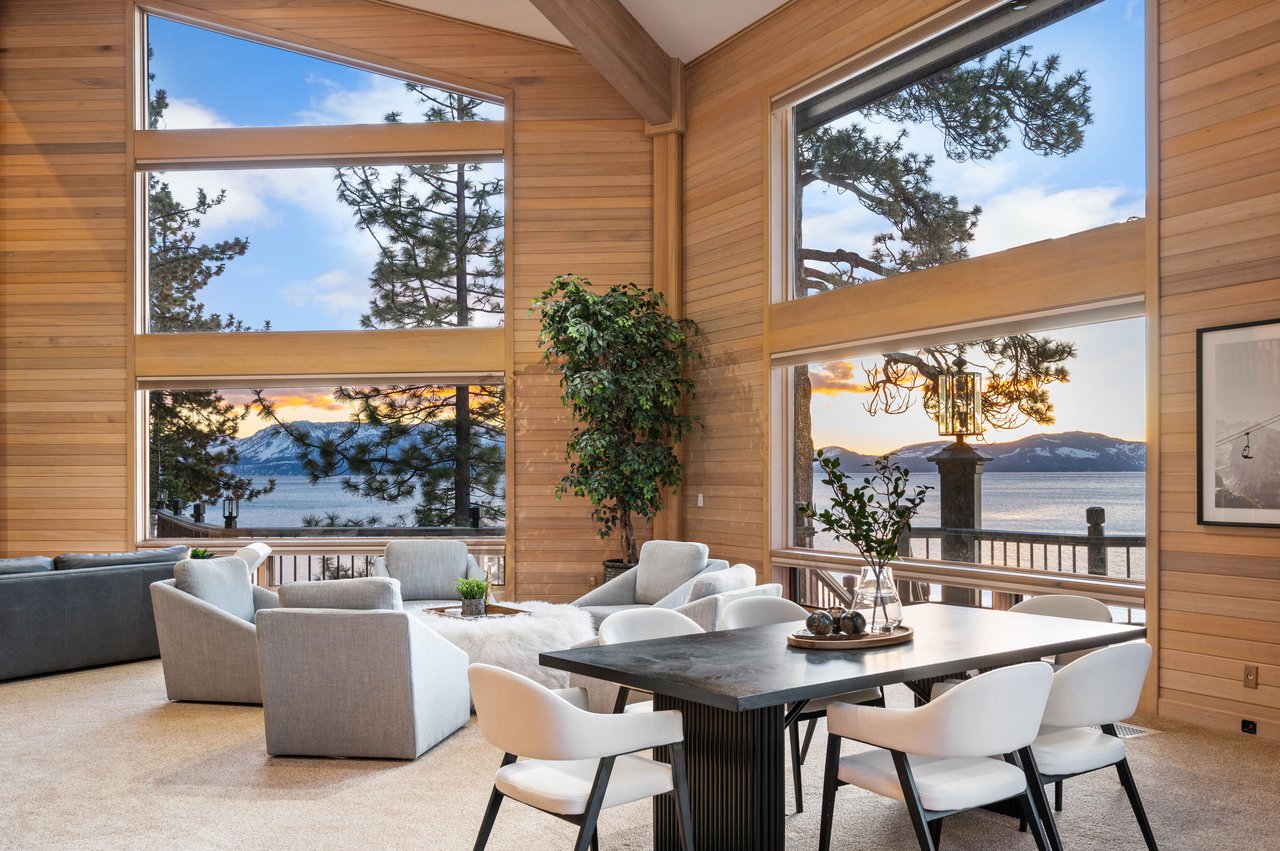 Wood-paneled living and dining area with large windows overlooking a lake and mountains.