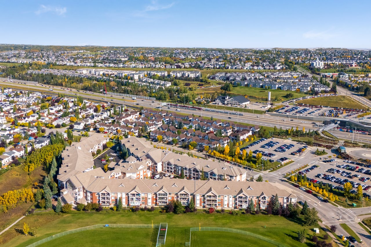 Aerial view of a condominium complex beside a sports field, highway, and residential neighborhoods.