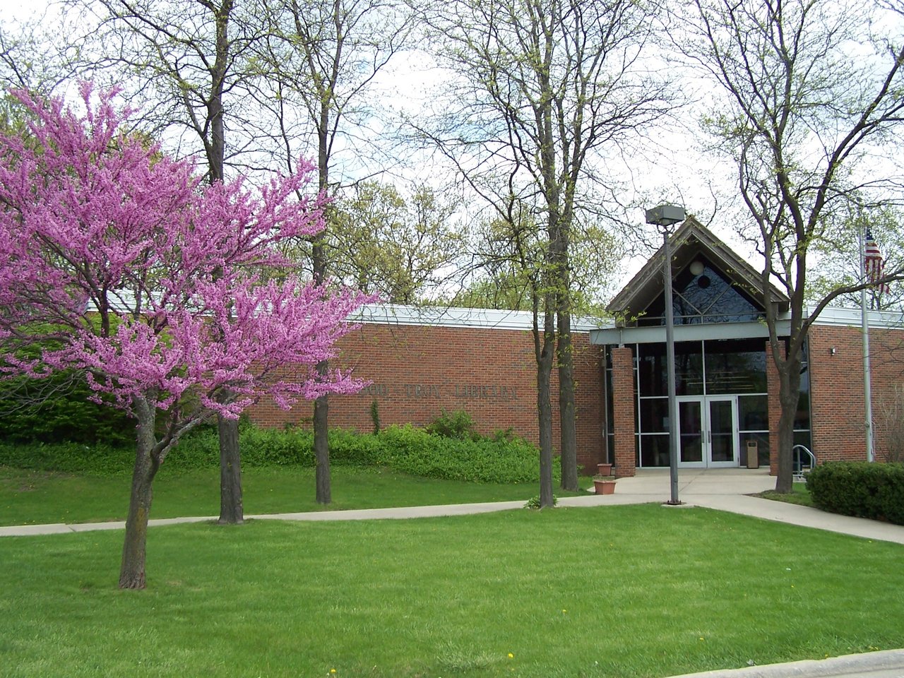 The brick Shorewood-Troy Public Library with a redbud tree in pink bloom on a green lawn in Shorewood, Illinois