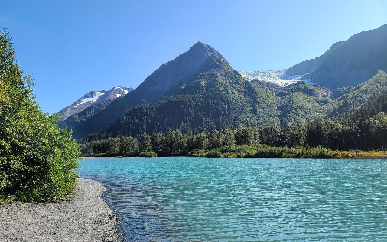 Turquoise lake below forested mountains and a glacier in Girdwood.