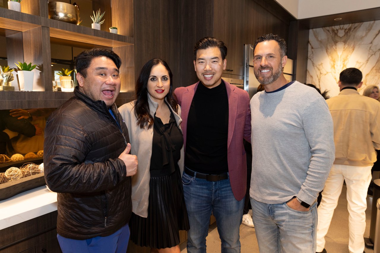 Four adults pose together at an open house in a modern kitchen showroom.