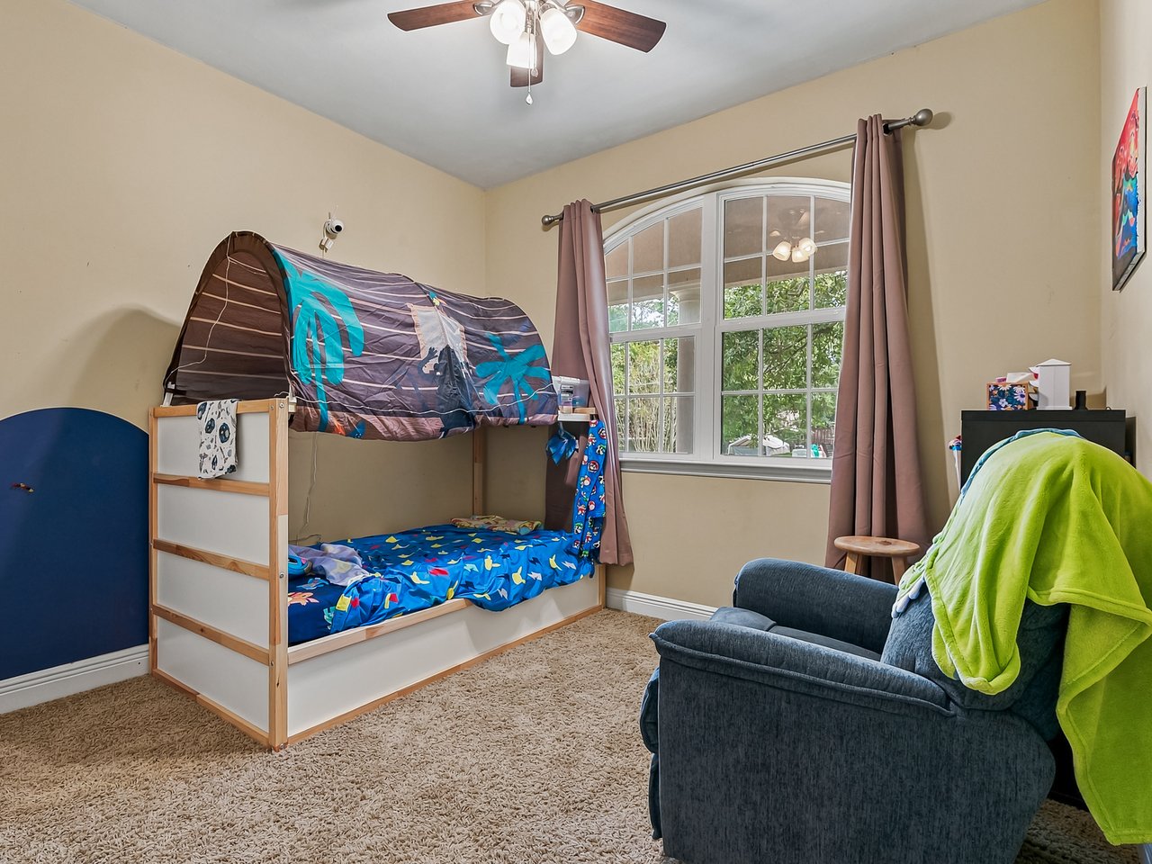 Bedroom with a canopied bunk bed, arched window, and armchair draped in a bright green blanket.