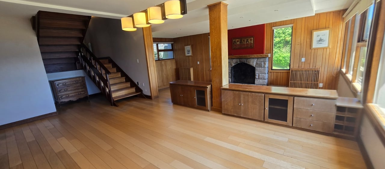 Living area with a stone fireplace, wood-paneled walls, built-in cabinetry, and a dark wood staircase.