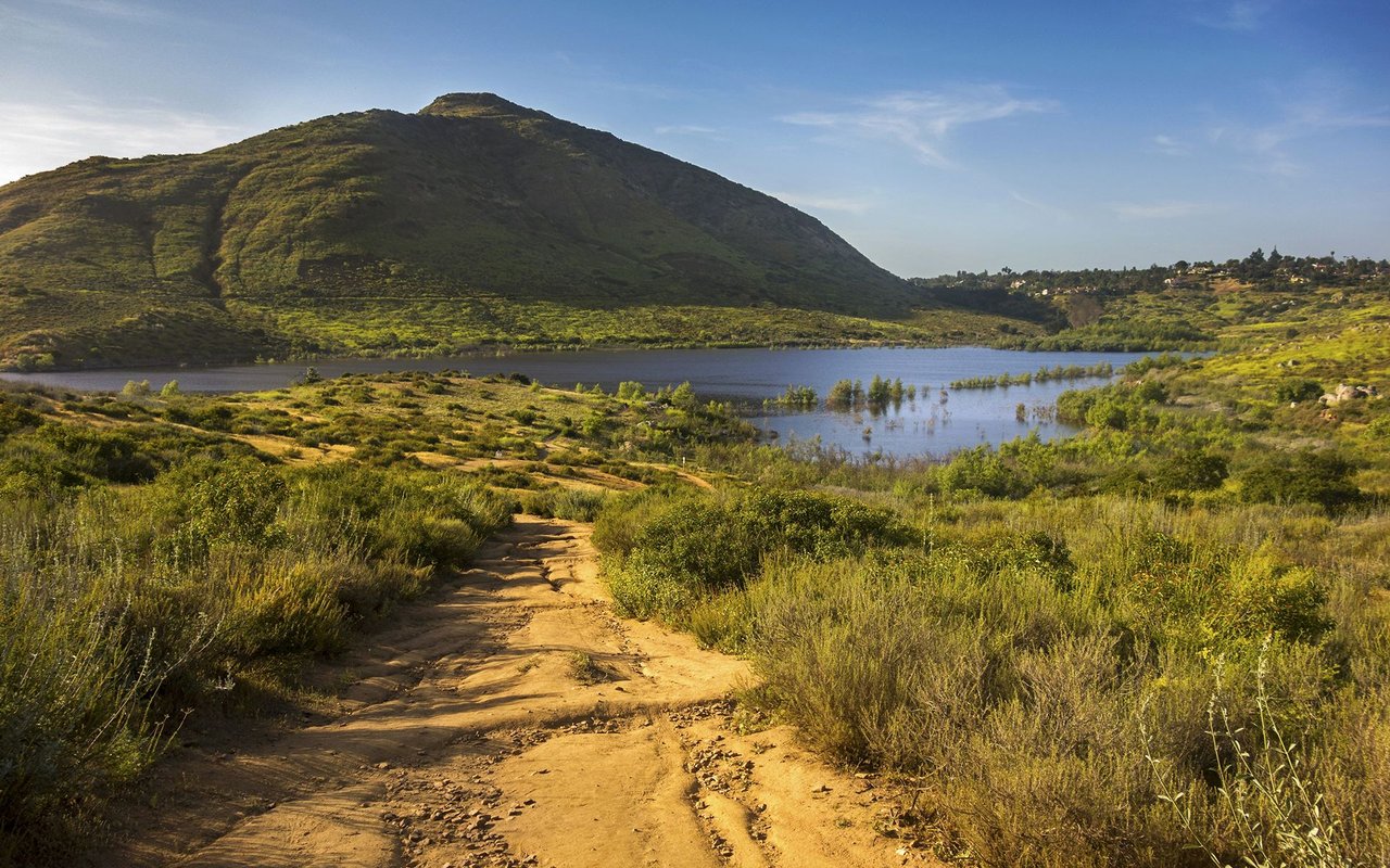 Rancho Bernardo trail winding through scrub toward a lake and hillside.