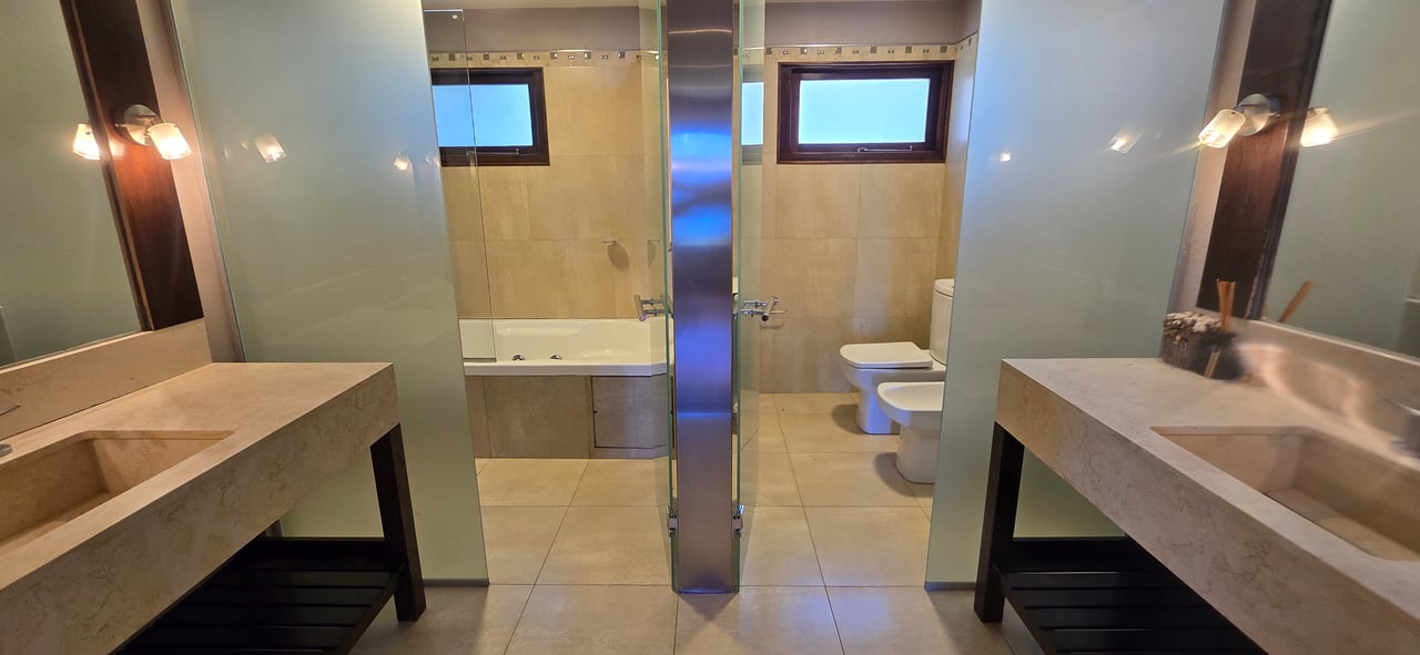 Bathroom with double stone vanities, glass-partitioned bathtub, and toilet and bidet.