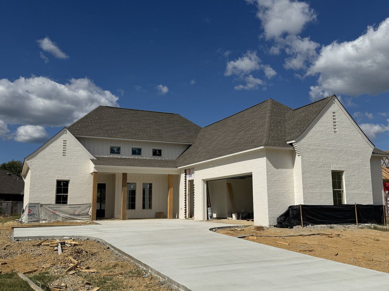 New white brick house under construction with an open garage and a fresh concrete driveway.