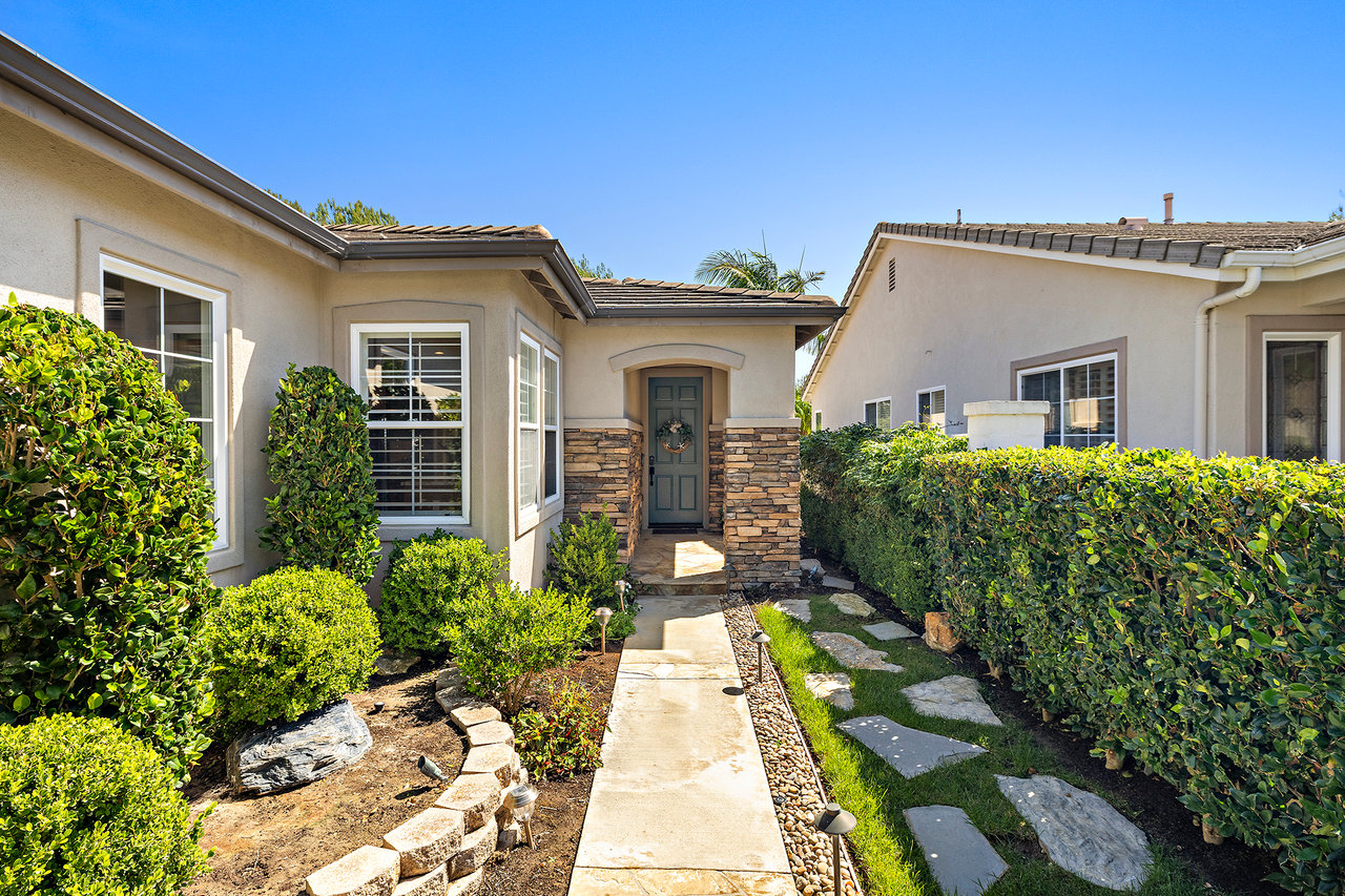 Home entrance with stone trim, a straight concrete walkway, and landscaped shrubs.