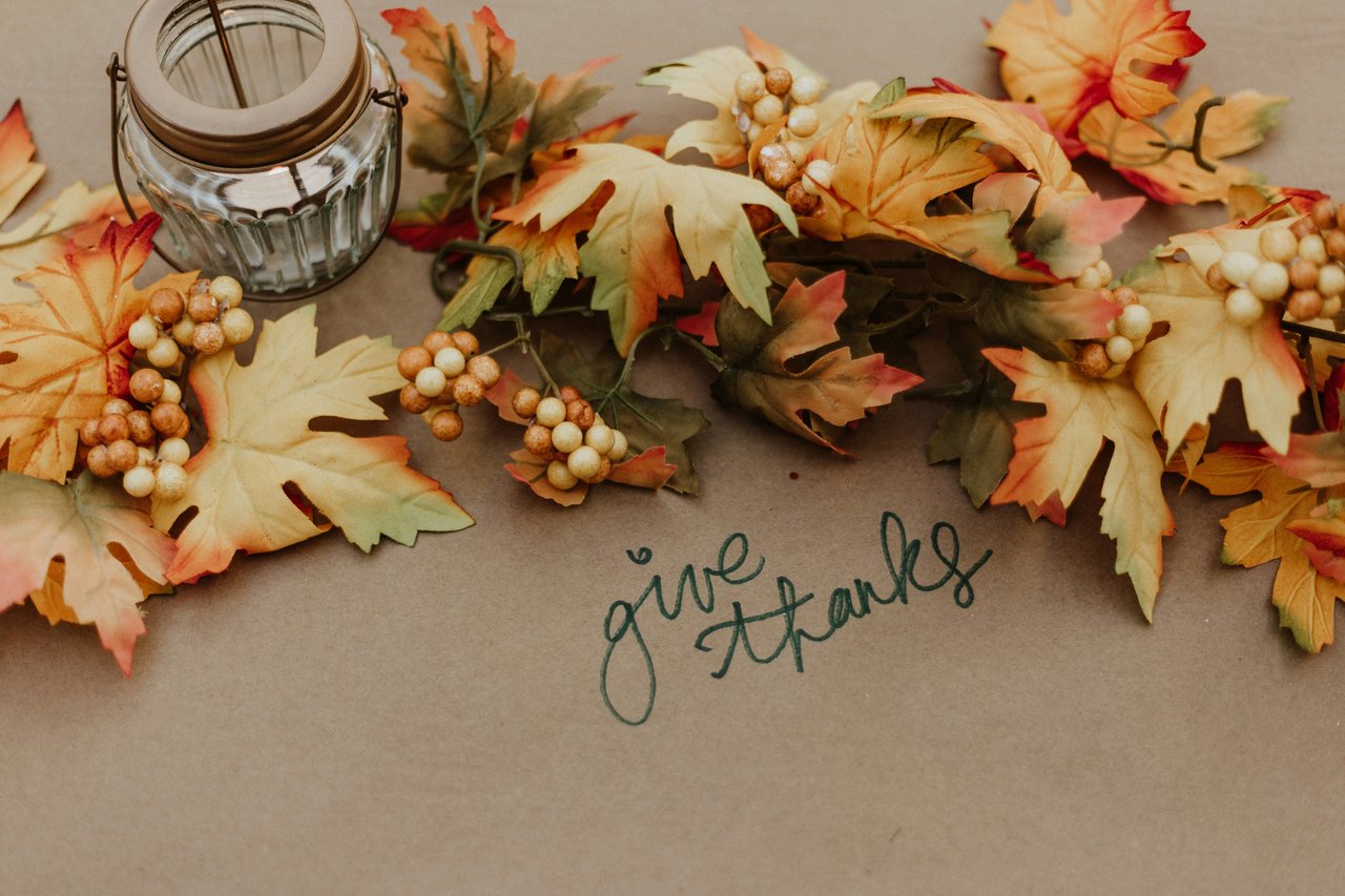 Autumn leaves and berries surround a glass jar and handwritten “give thanks” message.