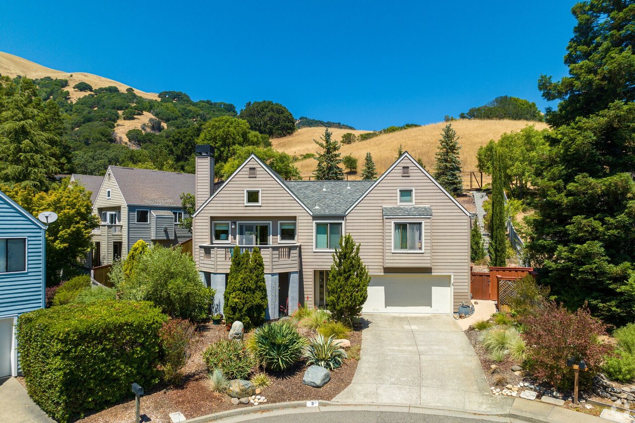 Beige two-story home with a front balcony and garage, backed by dry hills.