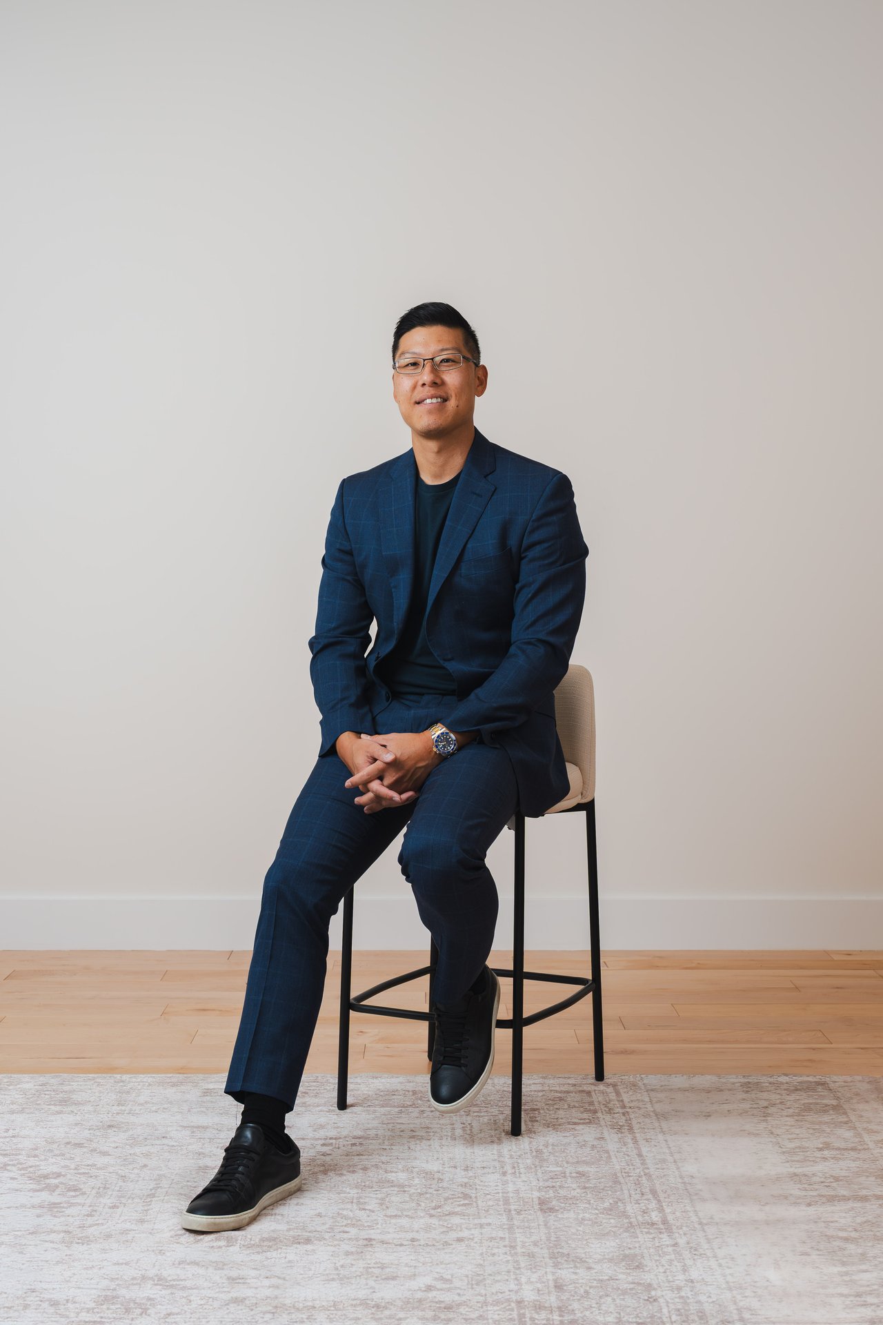 Eddie Chon seated on a stool in a navy suit and black sneakers.