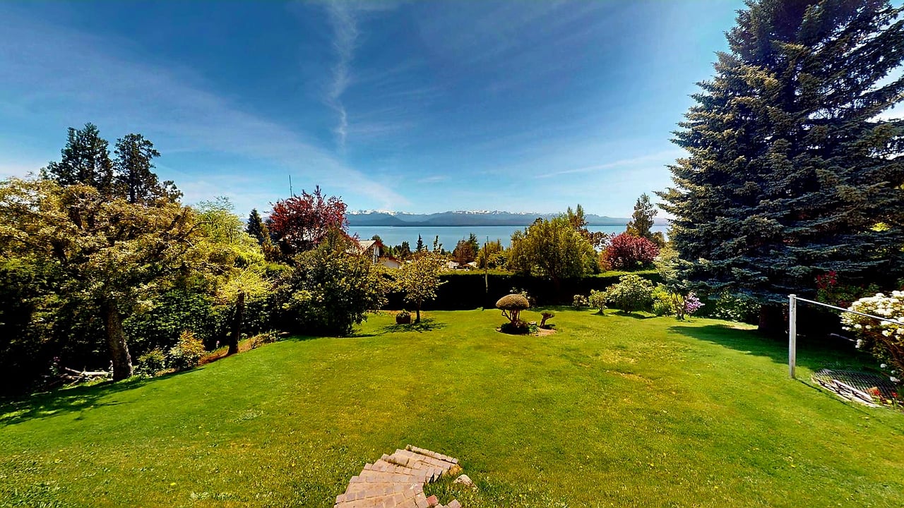 Landscaped lawn with ornamental trees, a lake, and distant snow-capped mountains.
