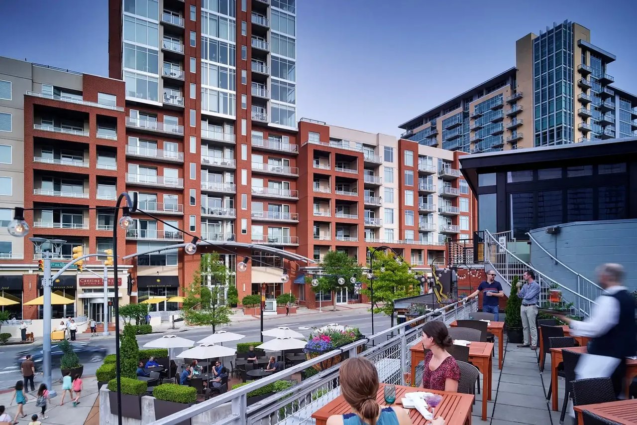 Modern apartment buildings with balconies overlook a lively outdoor dining terrace.