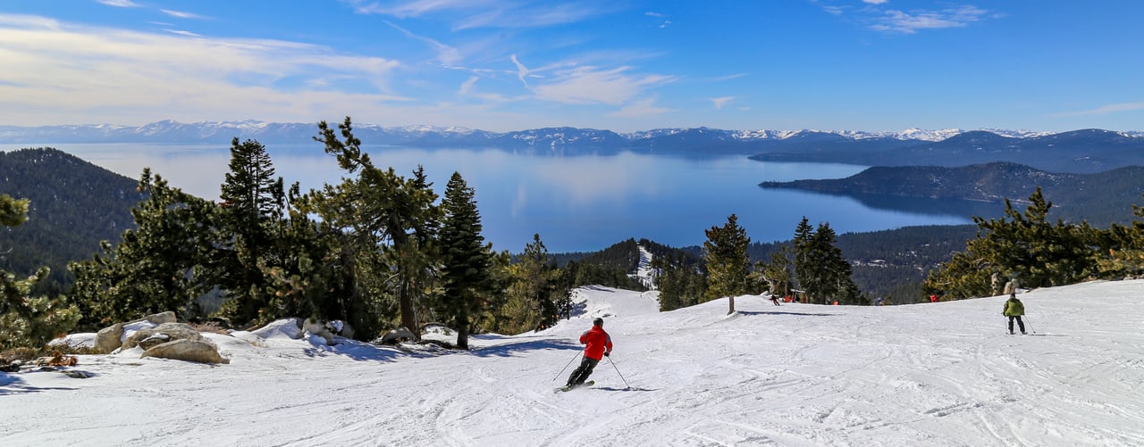 A stunning view of a skier gliding down the slopes at Diamond Peak Ski Resort, with the sparkling blue waters of Lake Tahoe in the background near Incline Village