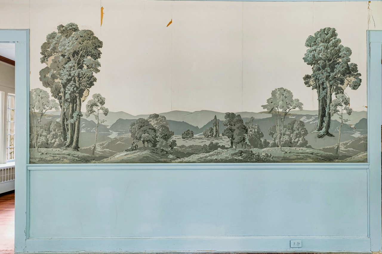 Pale blue room with a large landscape mural above matching wainscoting.