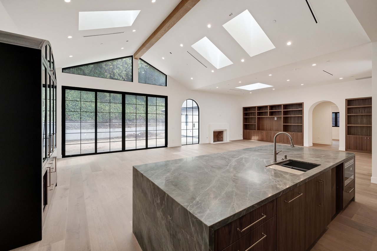 Spacious kitchen with a gray stone island, skylights, and black-framed glass doors.