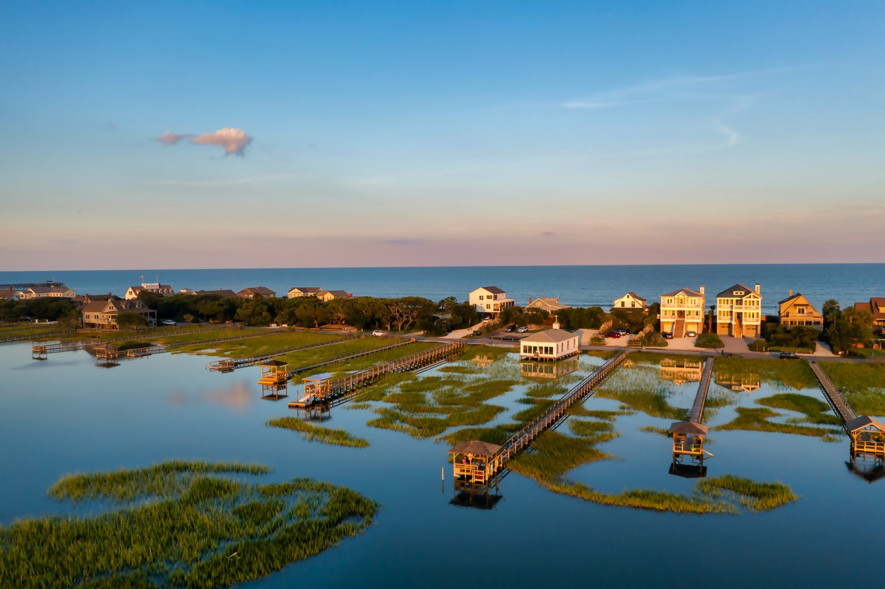 Coastal homes and docks along a marsh beside the ocean at sunset.