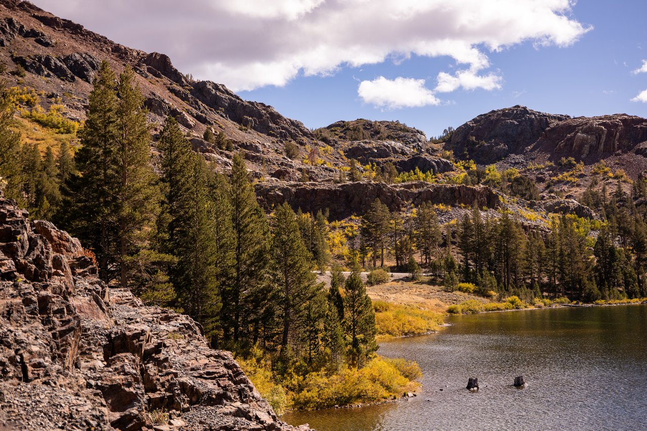 Rocky mountain lake bordered by pine trees and golden autumn vegetation.