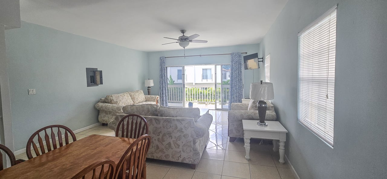 Furnished living and dining area with floral sofas and sliding doors to a balcony.