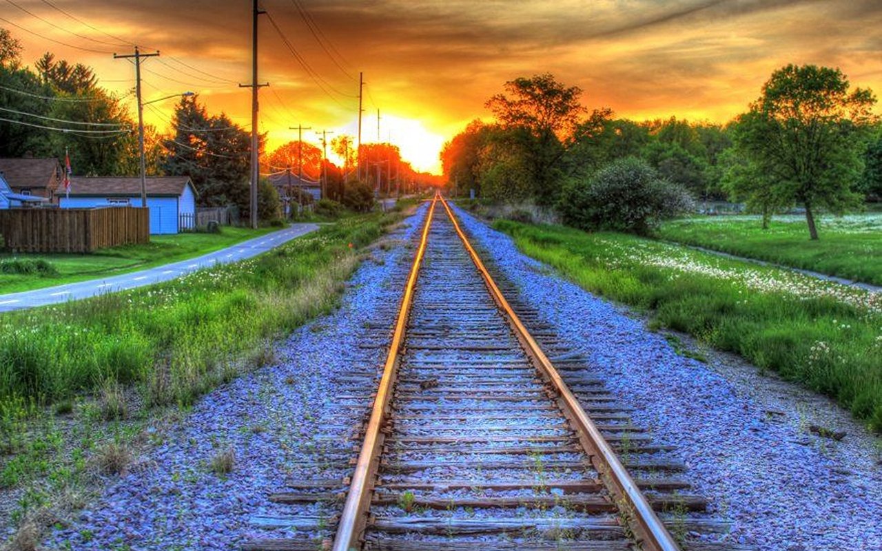 Railroad tracks run through a grassy neighborhood toward a vivid sunset.