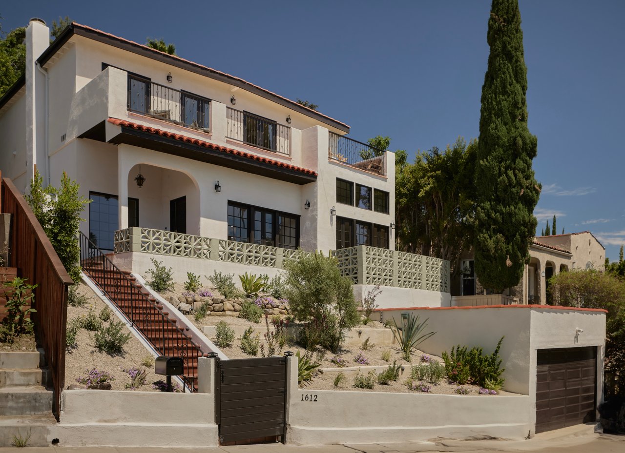 Spanish-style home with red tile roof, wrought-iron balconies, sloping garden, and front gate.