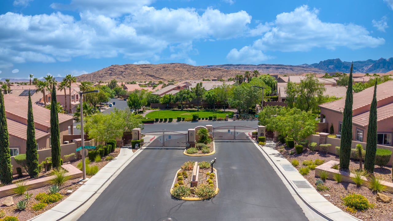 Gated residential community entrance with desert landscaping and mountains beyond.