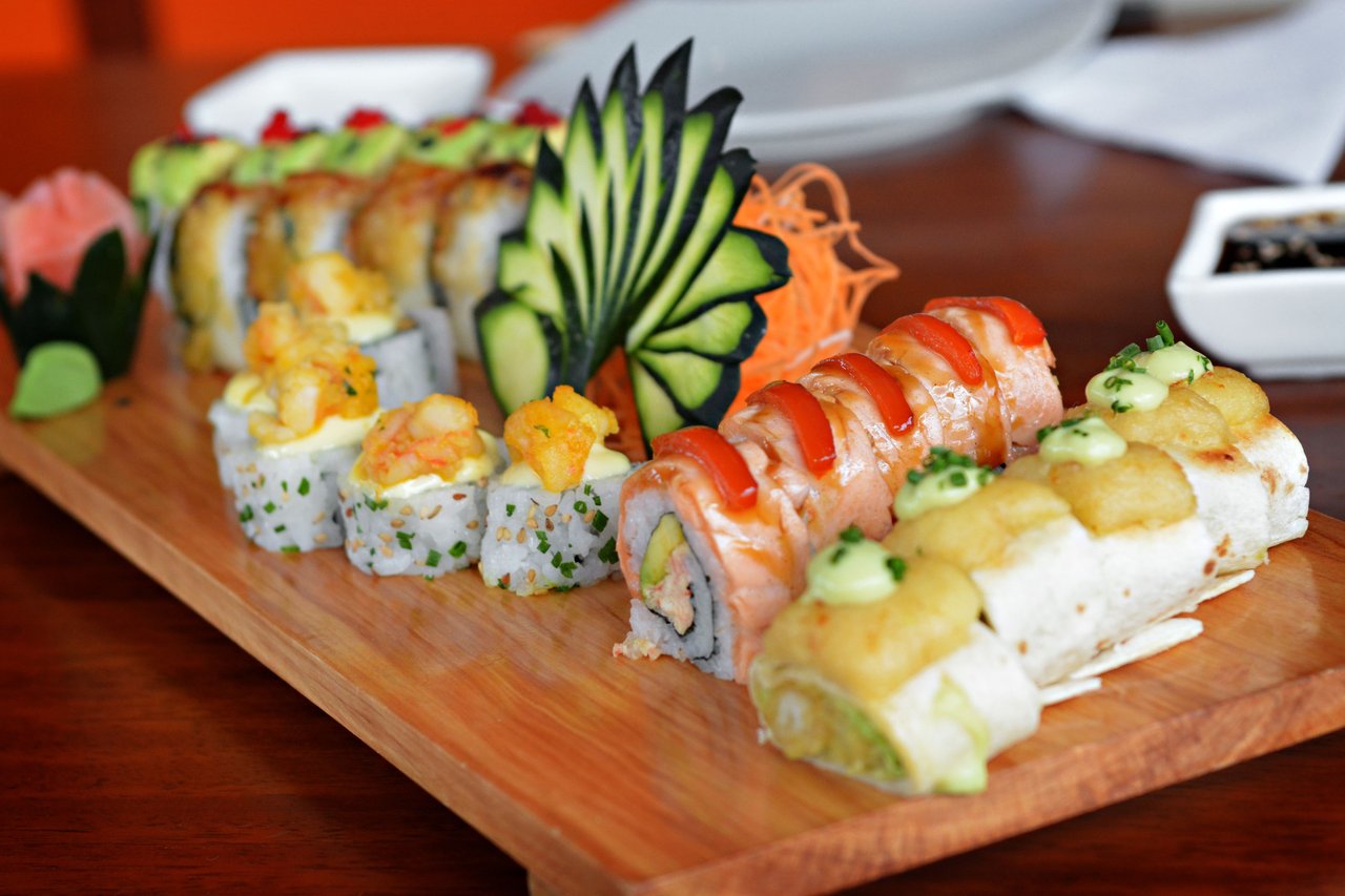 Assorted sushi rolls on a wooden board, with salmon, tempura, and cucumber garnishes.