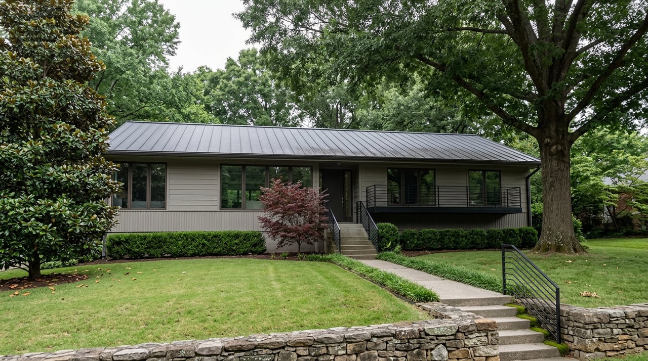 Two-story gray home with broad oak and magnolia canopies, balcony, and entry stairs above a sloping lawn.