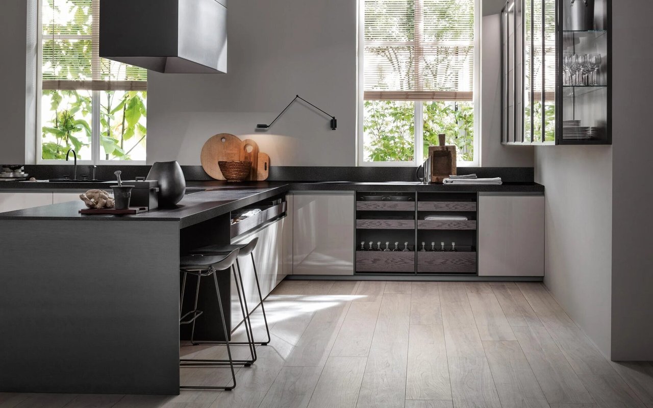 Modern kitchen with a dark island, pale cabinetry, open shelving, and tall sunlit windows.