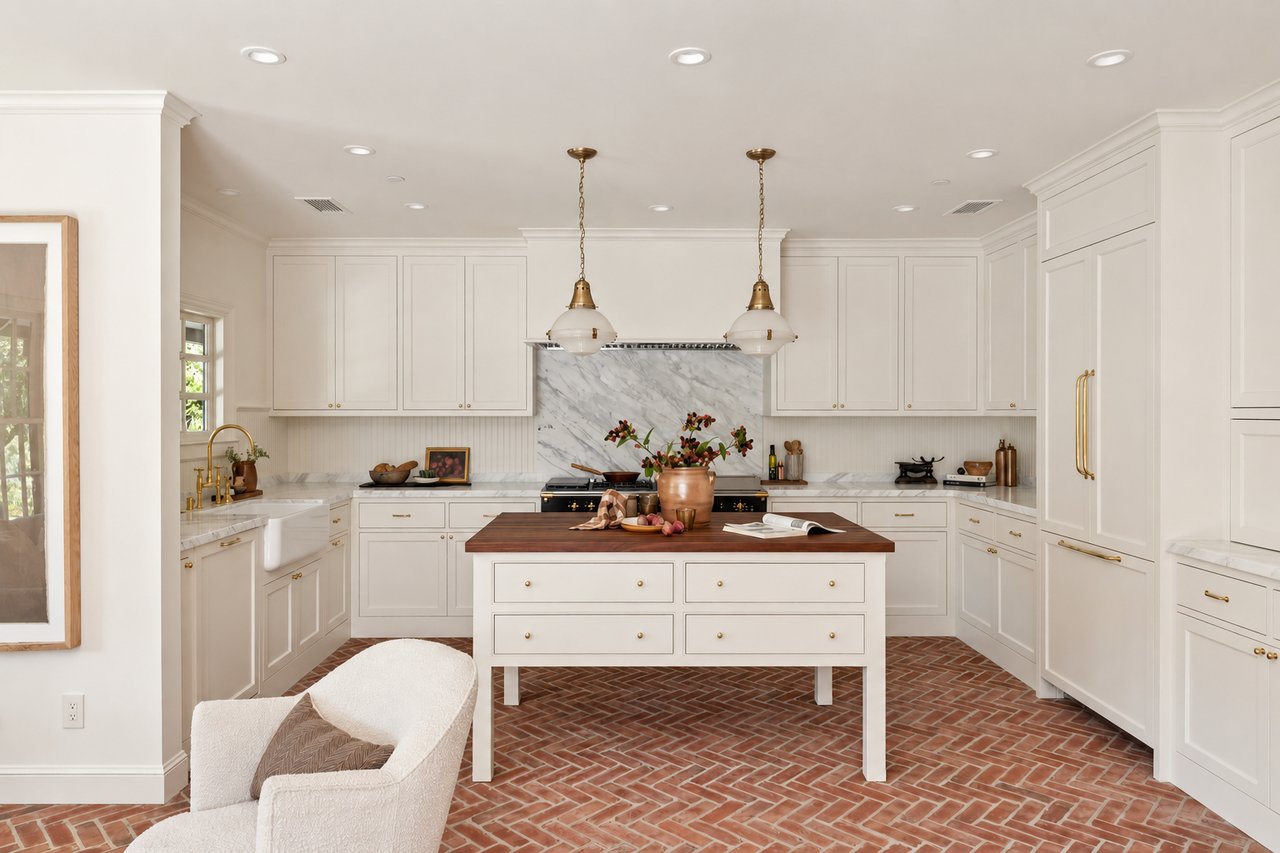 Bright white kitchen with marble backsplash, walnut island, brass fixtures, and herringbone brick floor.