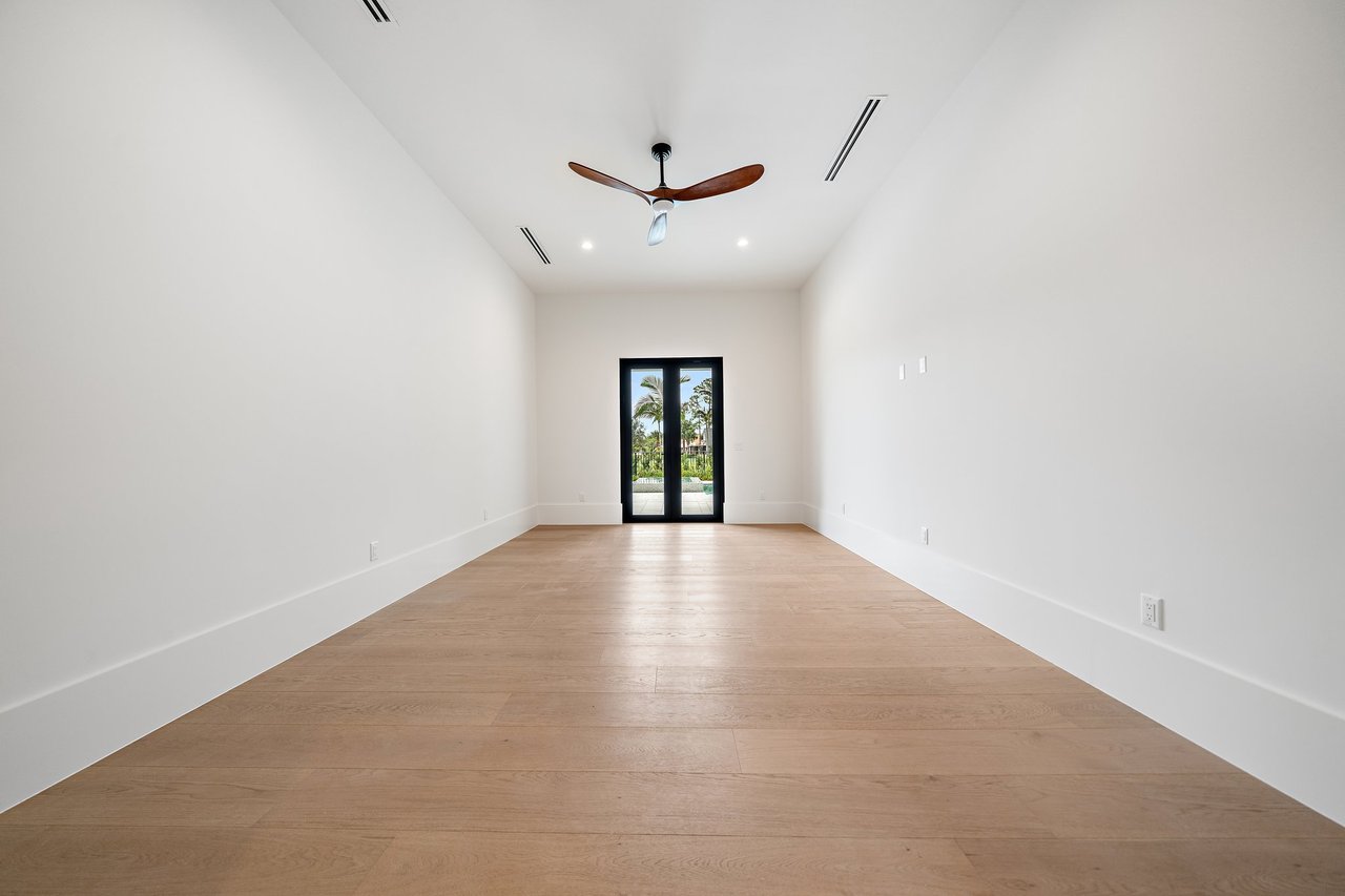 Empty room with light wood flooring, a wood-blade ceiling fan, and black-framed glass doors.