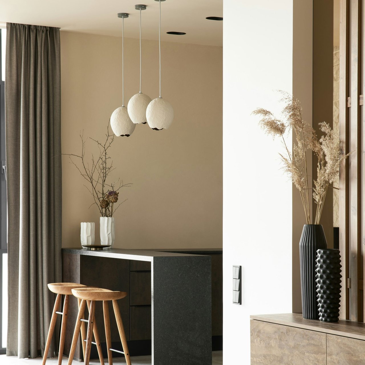 Modern kitchen with a dark stone island, wooden stools, and sculptural pendant lights.