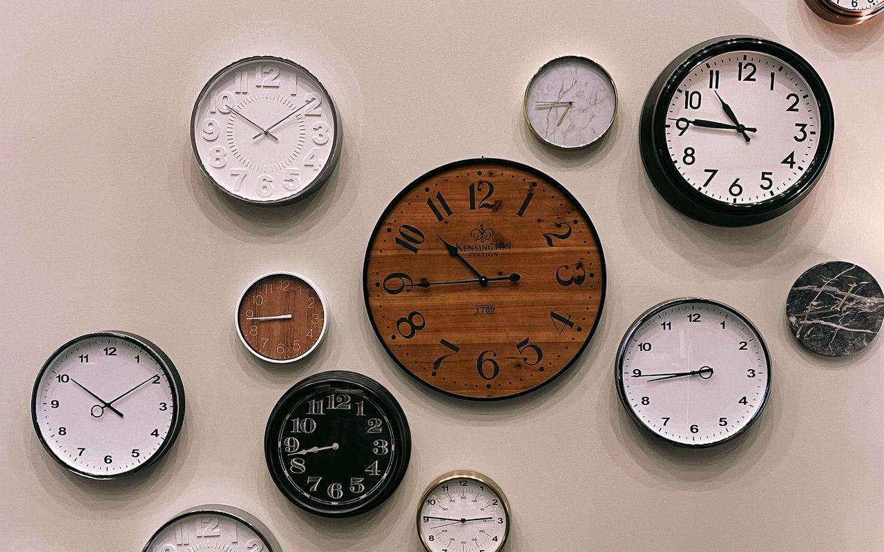A wall of assorted clocks, centered around a large wooden Kensington Station clock.