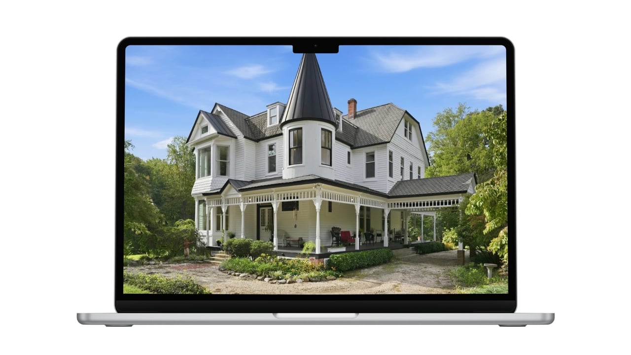 White Victorian house with a tall turret, wraparound porch, and landscaped grounds.