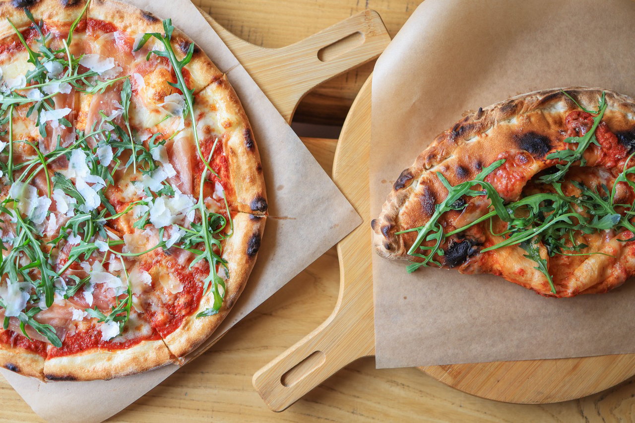 Two artisan pizzas topped with tomato, cheese, and arugula on wooden boards.