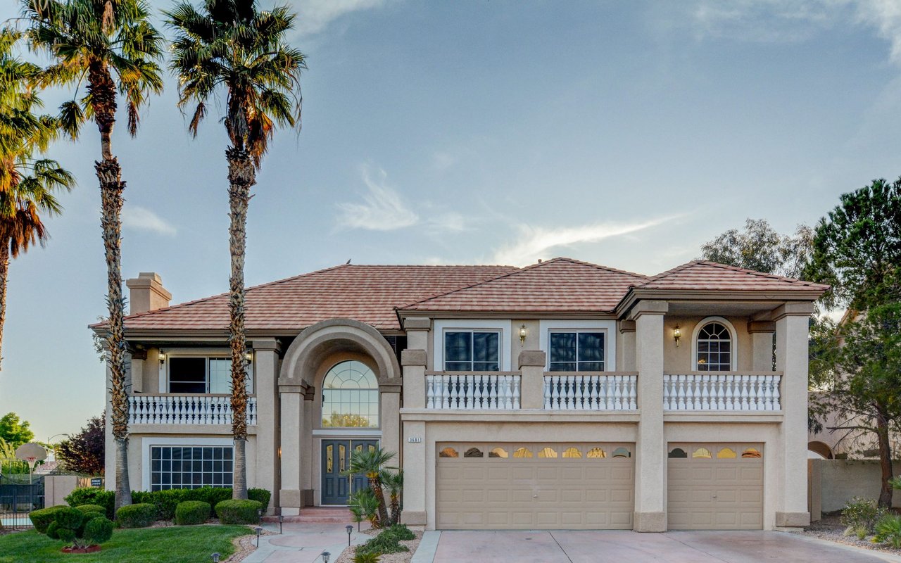 Two-story stucco home with a red tile roof, arched entry, balconies, and palm trees.