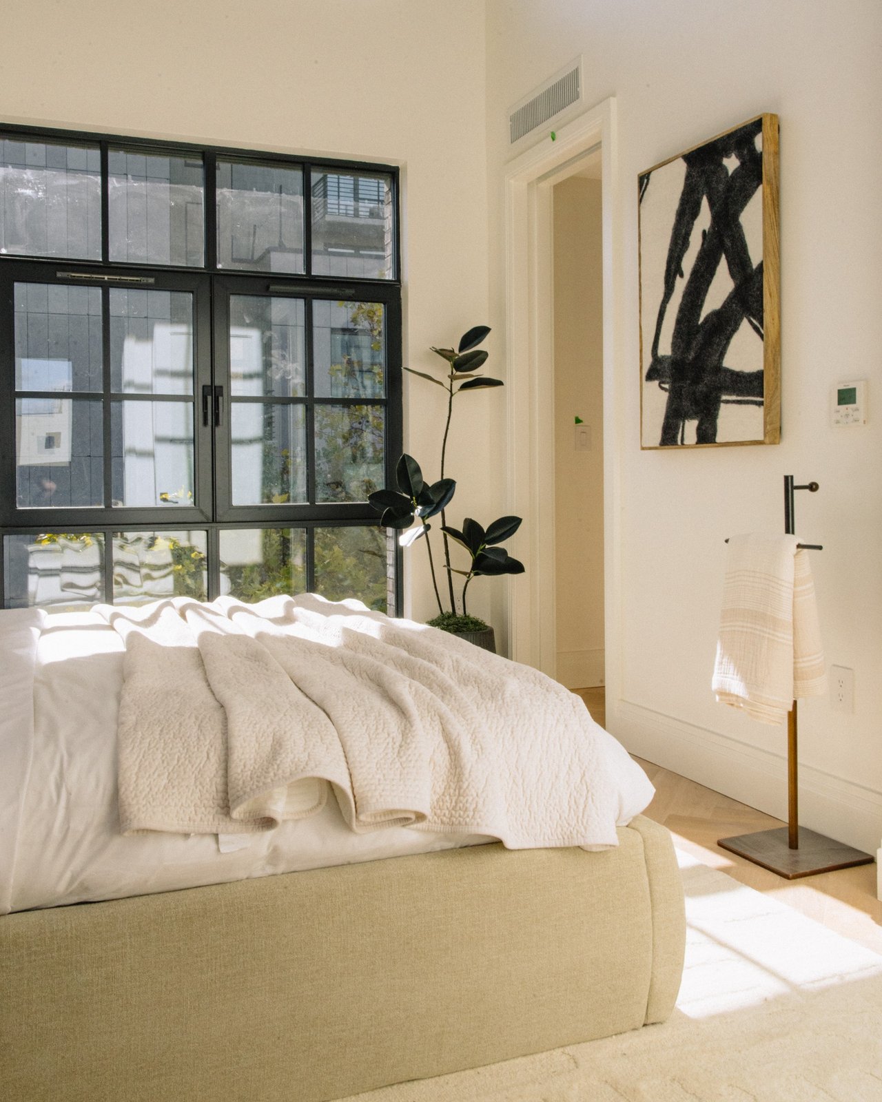 Bedroom with a low upholstered bed, large black-framed windows, and abstract wall art.