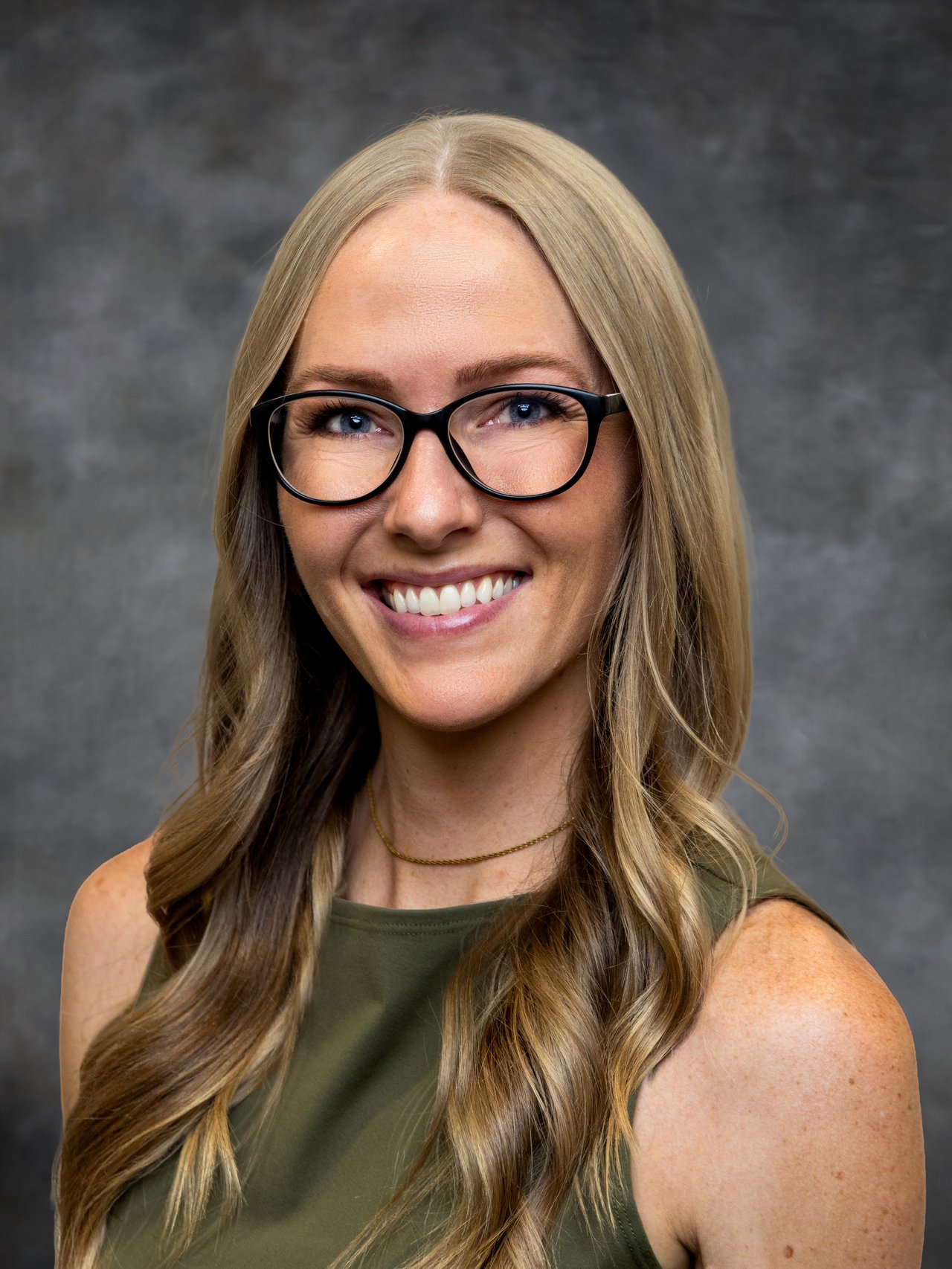 Danielle Carlston smiling in black glasses, with long blonde hair and a dark olive top.