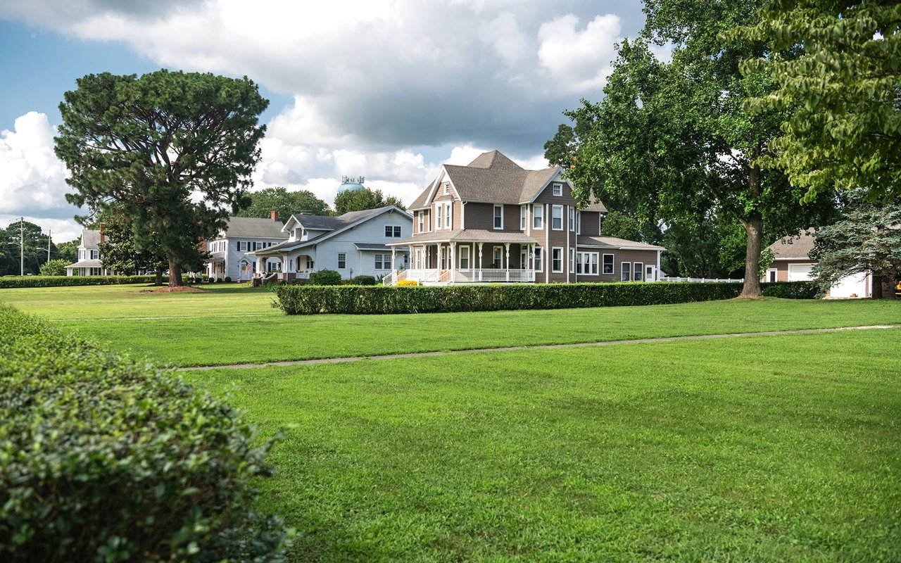 Neighborhood homes behind a broad lawn, with a two-story house featuring a wraparound porch.