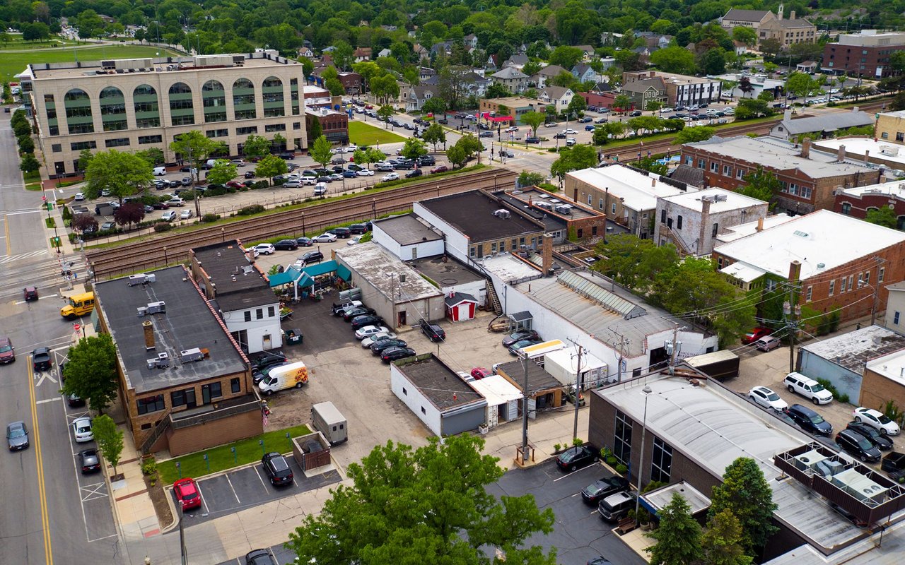 Aerial view of a downtown commercial district with railroad tracks and leafy streets.