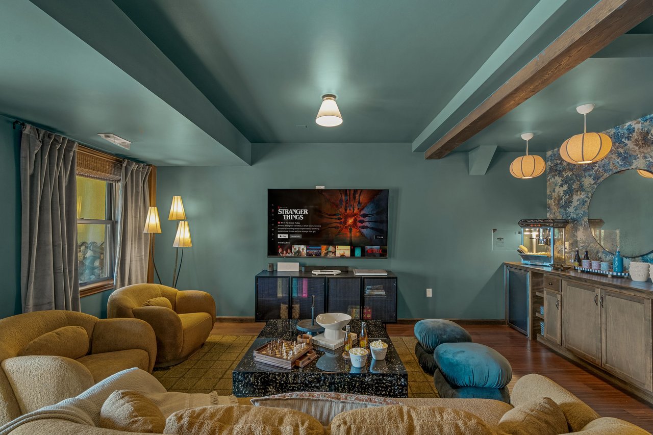 Furnished living room with teal walls, mustard seating, a wall-mounted television, and a game table.