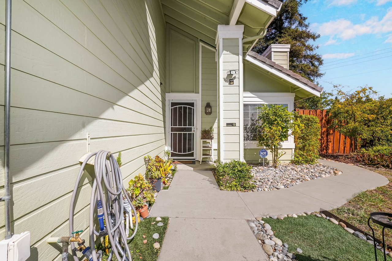 Home entrance with a security screen door and curved walkway bordered by shrubs and river rocks.