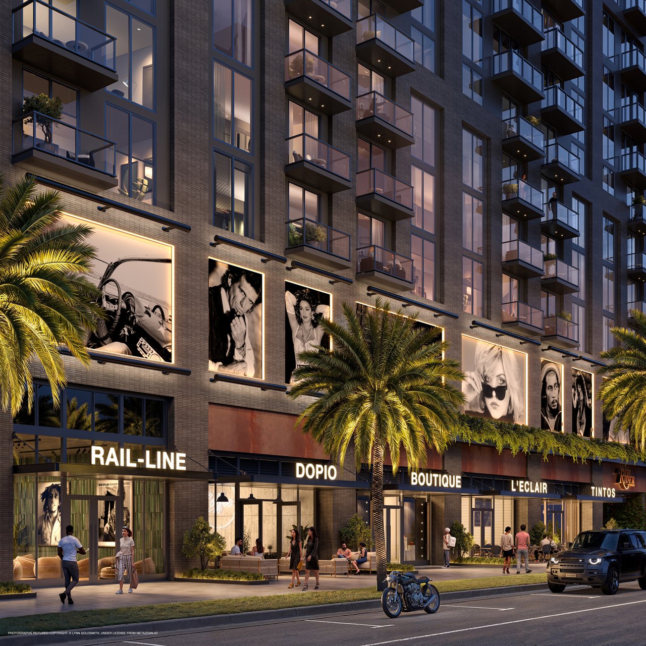 The Rider Residences exterior at dusk, with glass balconies, illuminated shops and palm trees.