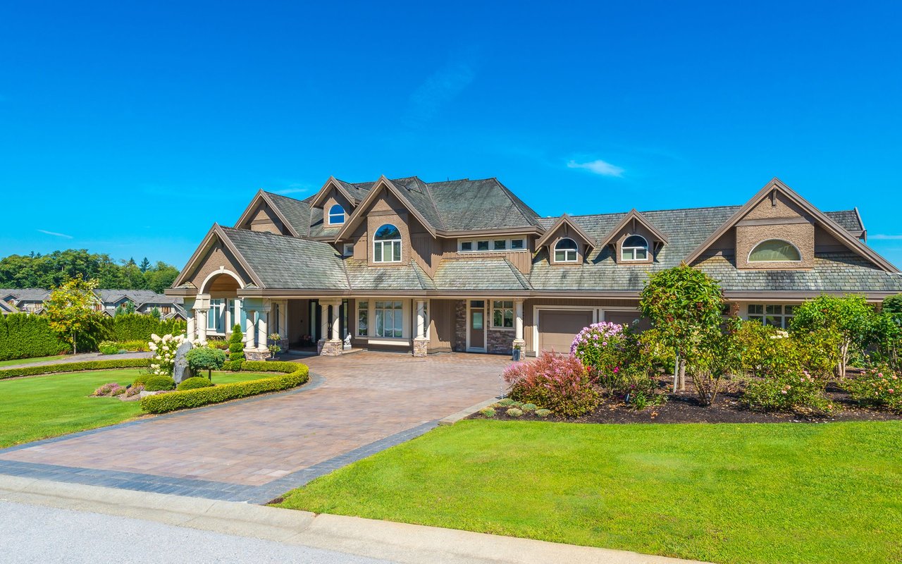Large multi-gabled house with a landscaped garden and wide paved driveway.