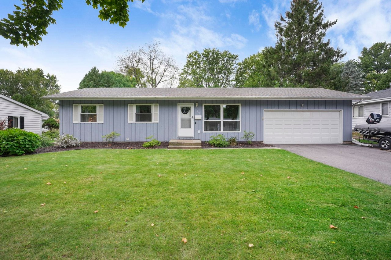 Single-story ranch home with blue-gray siding, a white attached garage, front entry steps, and a lawn bordered by planting beds.