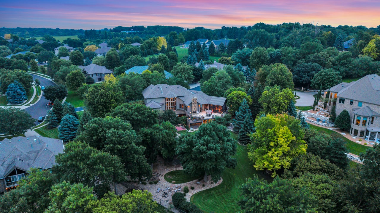 Aerial view of luxury homes nestled among mature trees beneath a pink dusk sky.