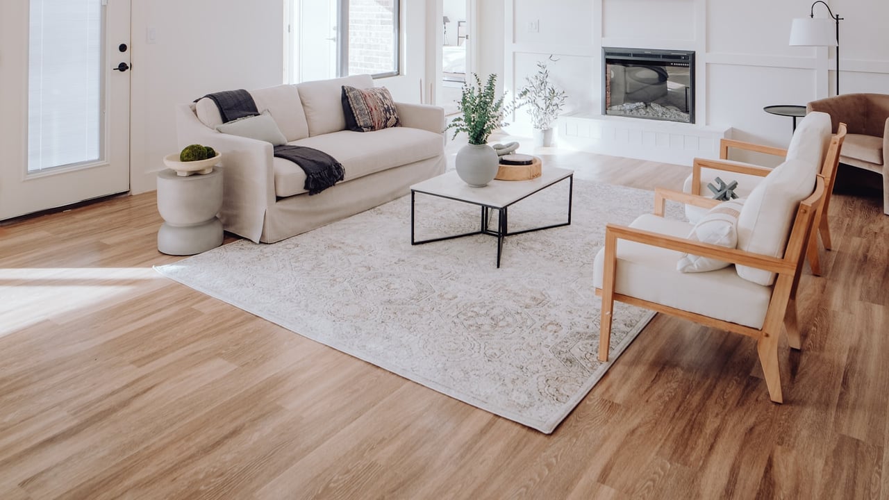 Staged living room with a white sofa, gas fireplace, and wood-framed armchairs on light wood floors.