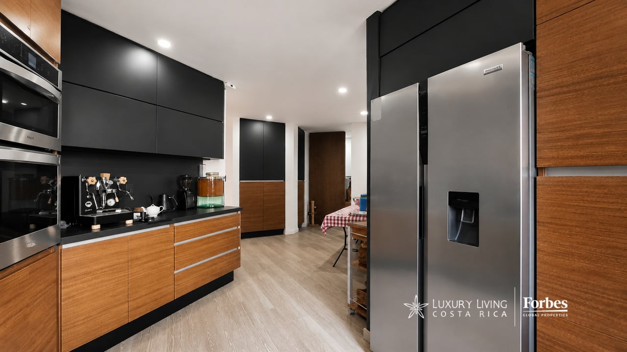 Modern kitchen with black cabinets, warm wood cabinetry, stainless steel appliances, and a coffee station.