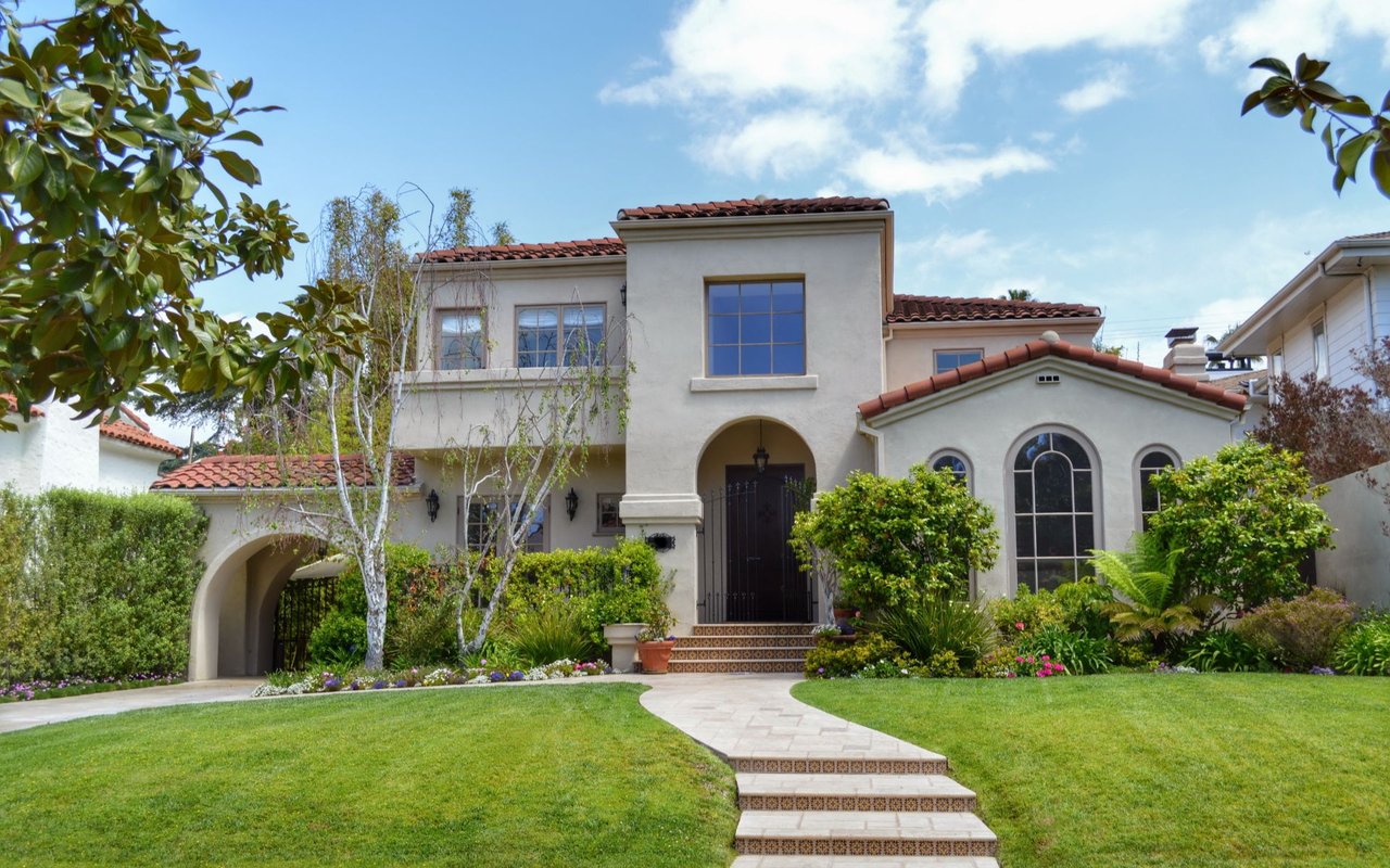 Two-story stucco home with a red tile roof, arched entry, and landscaped front lawn.