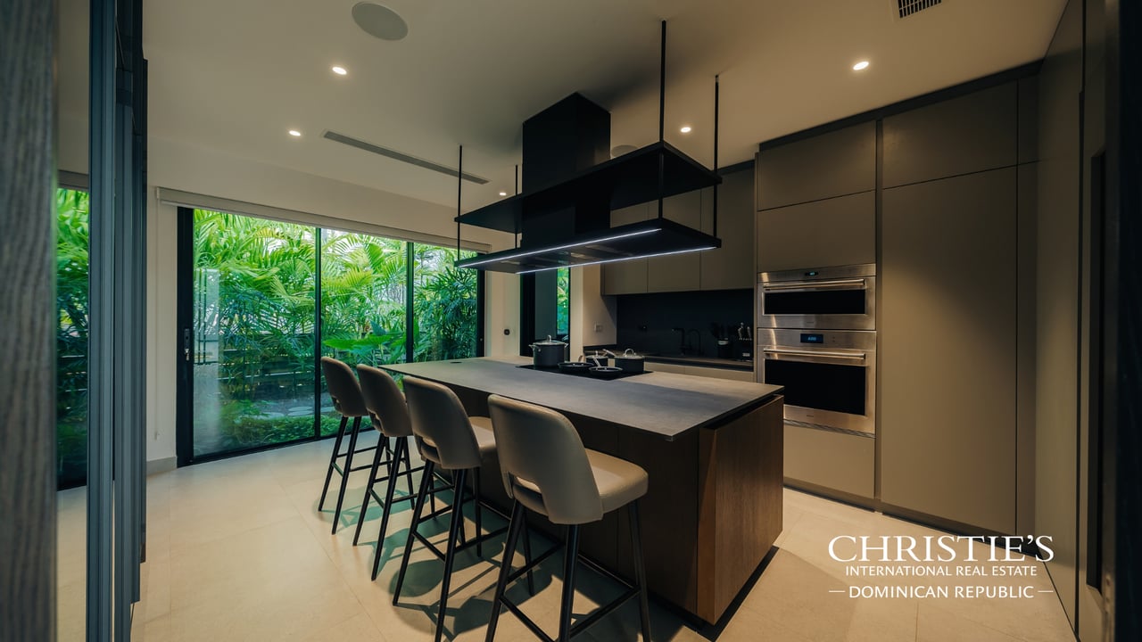 Modern villa kitchen with a large island, four bar stools, and garden-facing glass doors.