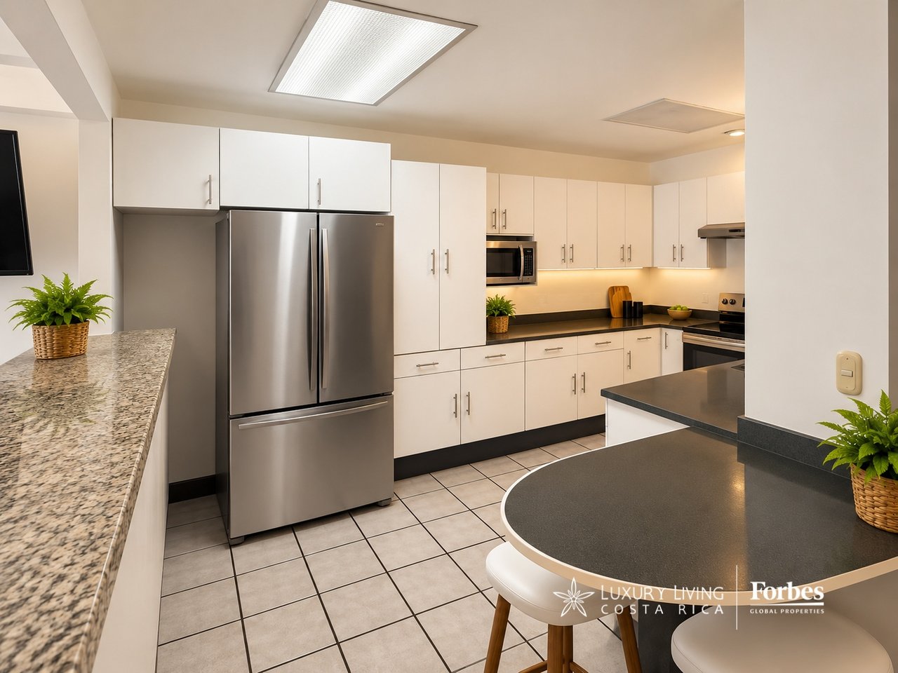 Modern kitchen with white cabinetry, stainless-steel refrigerator, dark countertops, and a rounded breakfast bar.